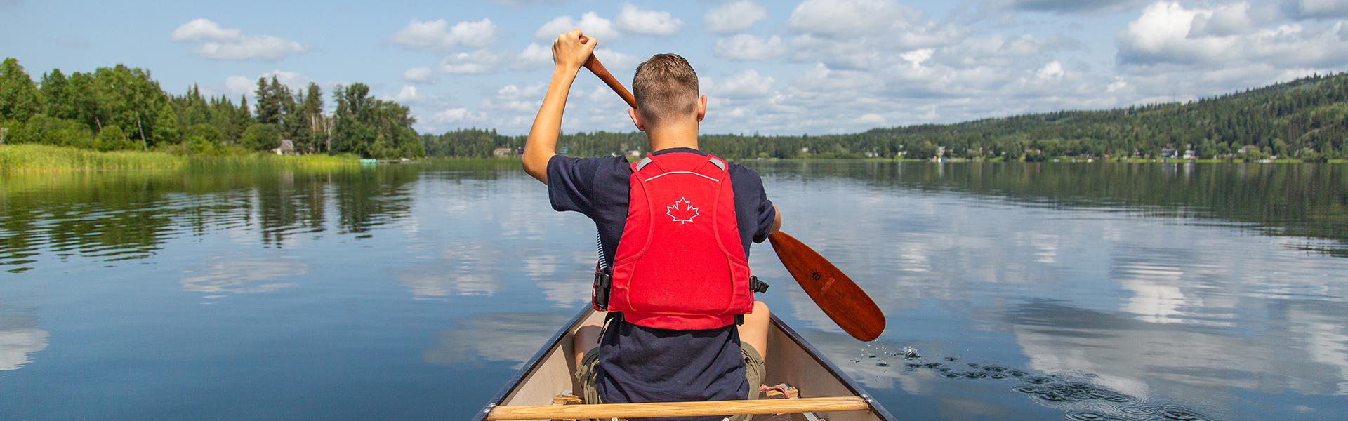 Man wearing a red life jacket canoeing on calm lake water