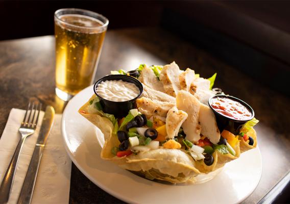 A plate of Taco salad with salsa and sour cream and glass of beer